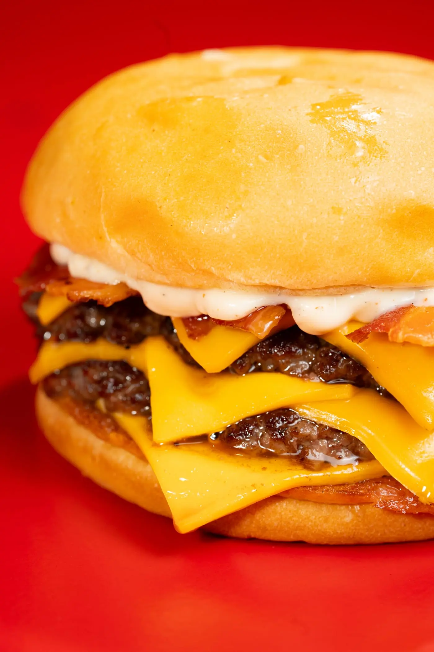 Primer plano de una hamburguesa con panceta, cheddar derretido y salsa blanca