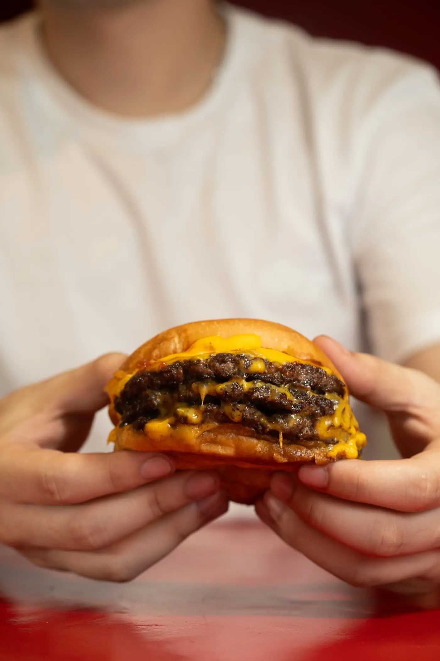 Manos sosteniendo una hamburguesa triple smash con queso